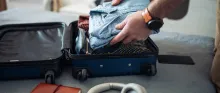 Un homme prépare sa valise de cabine avec des vêtements, un carnet de notes et des écouteurs.